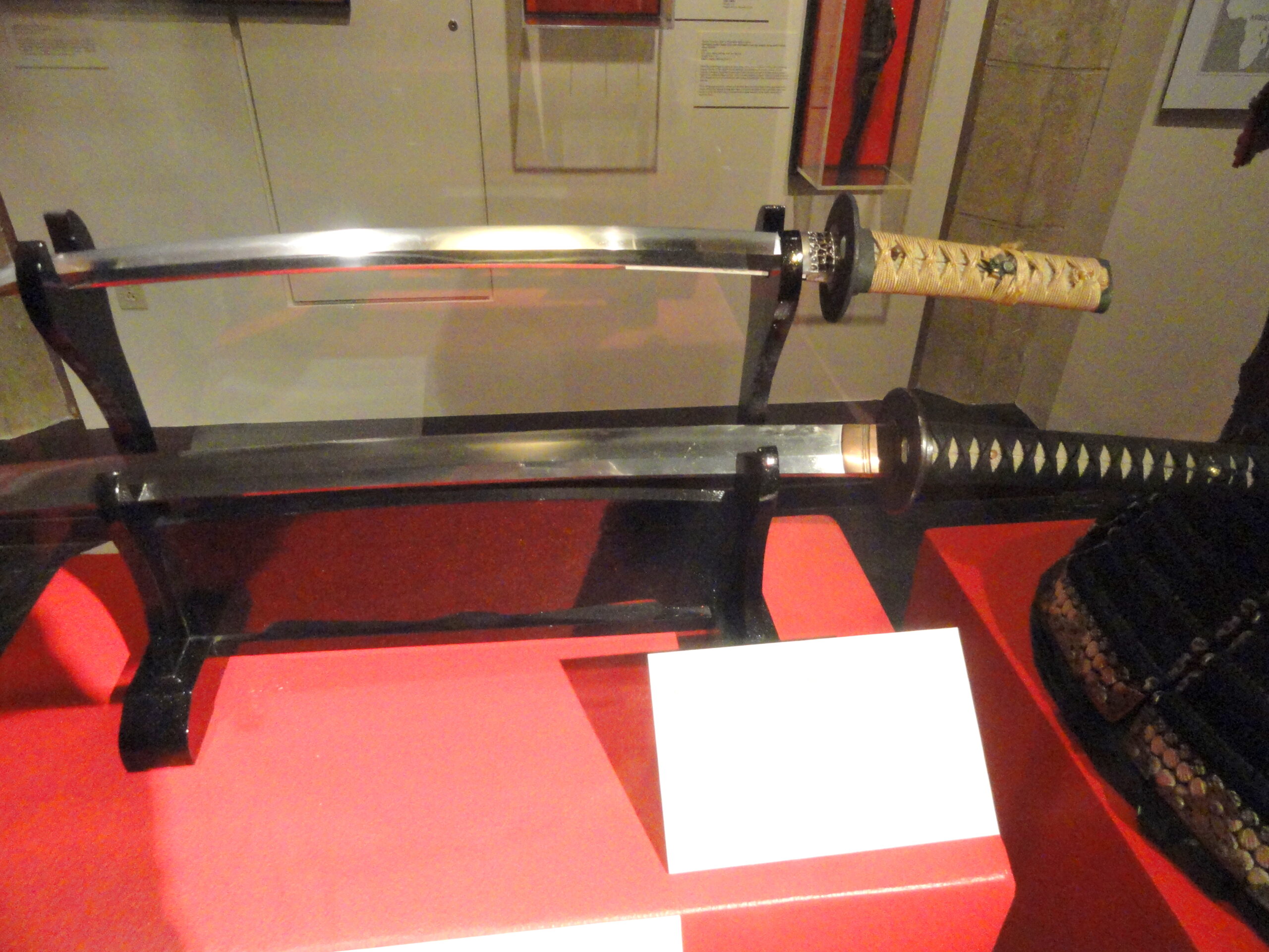 Várias espadas japonesas exibidas em prateleiras horizontais do museu Higgins Armory Museum, mostrando katana, wakizashi e tachi de vários períodos